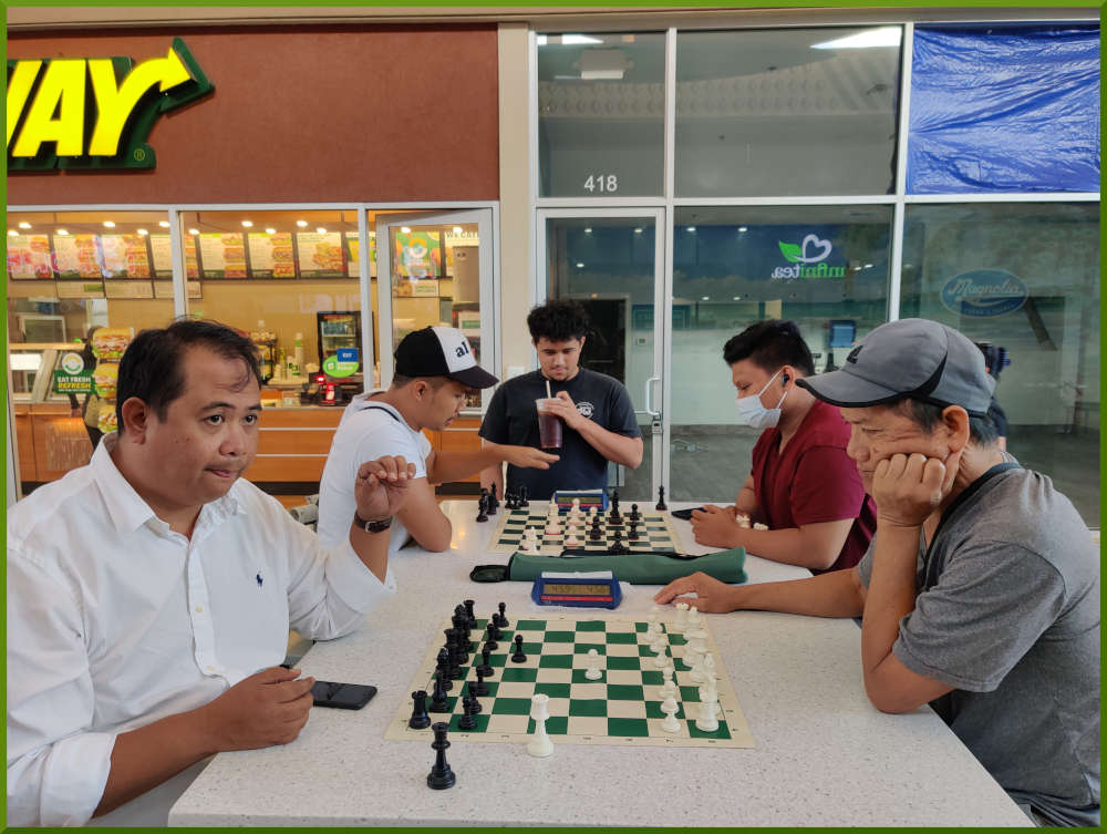April 19th, 2022. Ka Makana Alii chess meetup. Richard vs Edgar (near board). Shane vs Prince (far board). Christian watches while he waits to get on board.